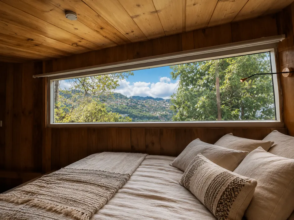 Cabin bed beside a wide window overlooking the hills