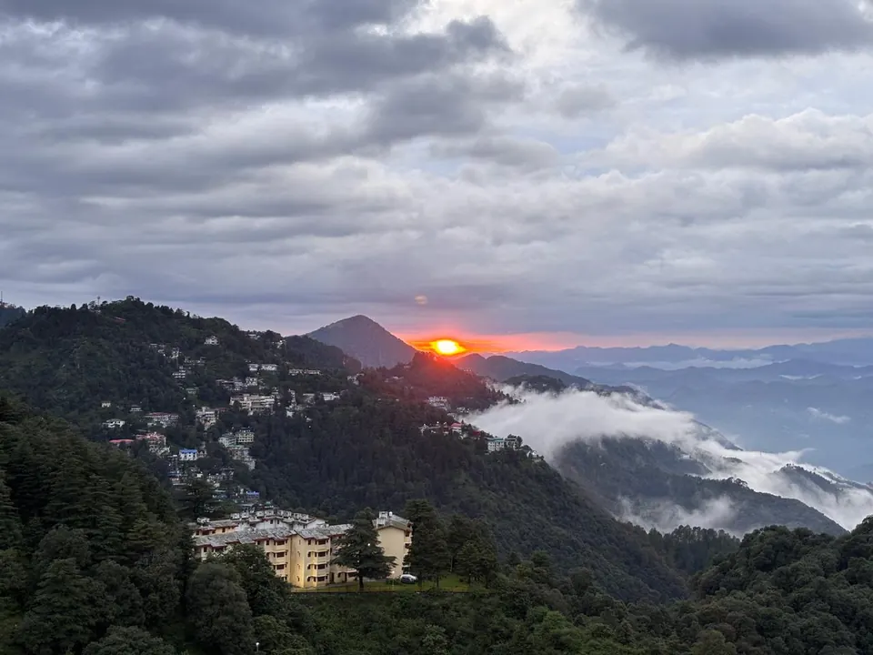 Sun setting behind green mountain ridges and low clouds