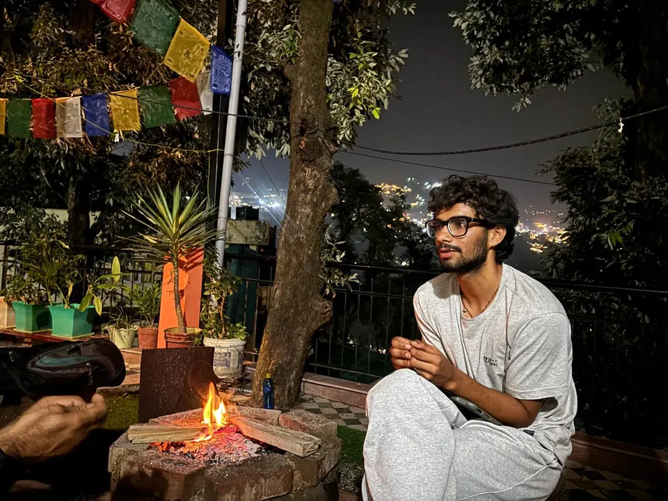 A guest sitting beside a terrace bonfire beneath prayer flags