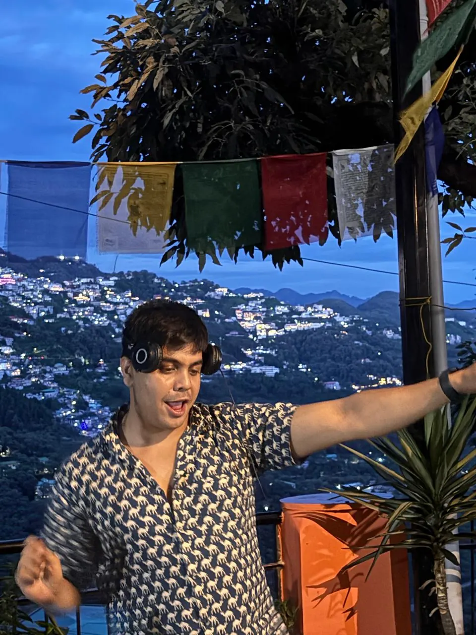 A guest wearing headphones on the terrace with hillside lights at dusk