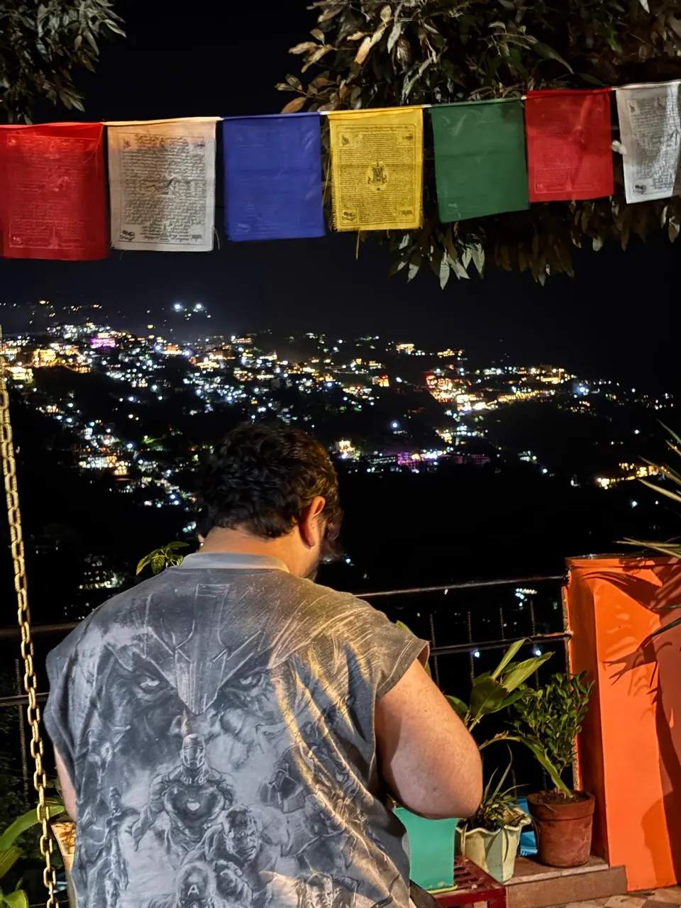 A guest on the terrace beneath prayer flags with the town lit up at night